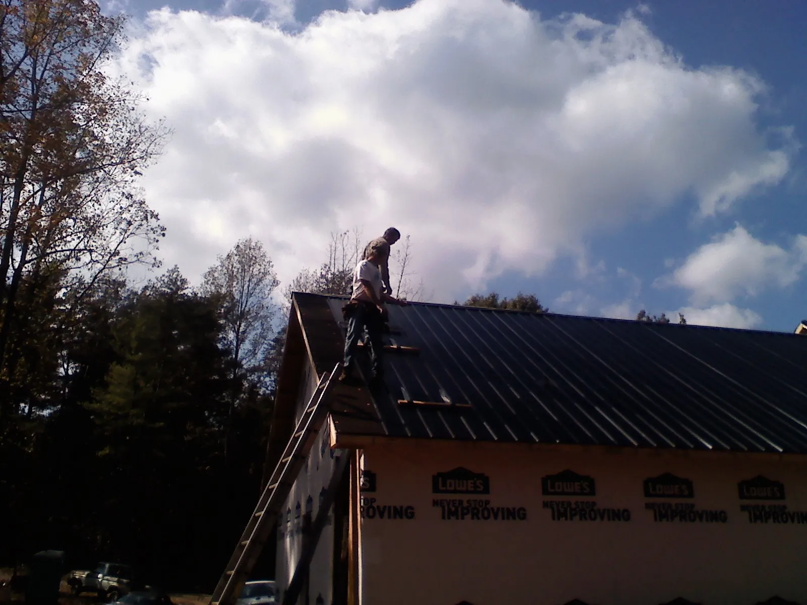 Roofer fastening dark metal panels high against a cloudy sky, from a Roof Inspection job in Highland