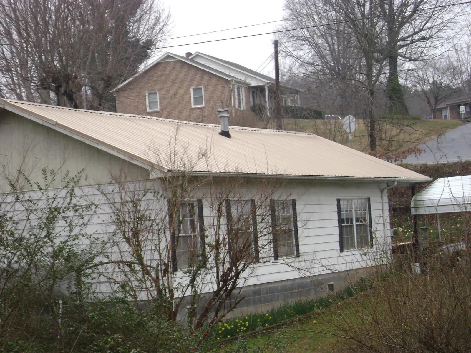 Tan metal roof on a white sided house set into a hillside — Commercial Roofing by Roofing Brothers in Highland